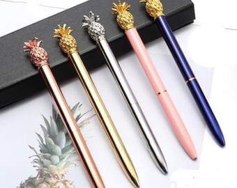 May include: Five gold pineapple-shaped pens with different colored barrels: pink, gold, silver, and blue. The pens are on a black surface.