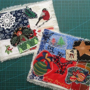 Op de afbeelding: Twee handgemaakte kerst-stofvierkanten met een verscheidenheid aan kleurrijke stofresten, waaronder een rode vogel, een sneeuwpop, een ster en een kerstboom. De vierkanten zijn aan elkaar genaaid met wit garen en hebben een rafelige rand.