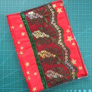 Può includere: Copertina di libro in tessuto rosso con stelle dorate e un bordo decorativo di paillettes dorate e perline marroni su uno sfondo bordeaux.