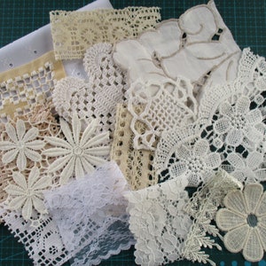 Op de afbeelding: Assortiment van witte en beige kantversieringen en doilies, sommige met bloemmotieven, op een groene snijmat.