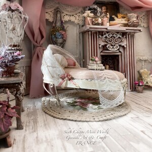 Könnte beinhalten: Eine Miniatur-Chaiselongue mit einem abgenutzten weißen Rahmen, beigem Stoffbezug und weißer Spitzenborte. Sie ist mit einem kleinen Blumenakzent verziert und steht auf einem runden Häkelteppich. Der Text "Shab Chippy Mini World Genuine Art & Craft FRANCE" ist sichtbar.