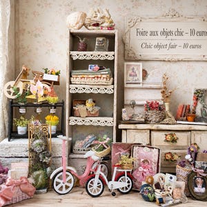 Könnte beinhalten: Eine Miniatur-Ausstellung mit einem hohen Holzregal mit Spitzenbesatz, einem rosa Fahrrad, einem weißen Fahrrad, einer Holzkommode und verschiedenen kleinen Dekorationsgegenständen. Ein Schild an der Wand lautet: Foire aux objets chic - 10 euros.
