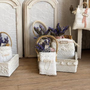 Könnte beinhalten: Eine Sammlung kleiner weißer Stoffbeutel mit Jutehenkeln, gefüllt mit getrockneten violetten Lavendelzweigen. Die Beutel sind mit zarter Spitzenborte und kleinen rechteckigen Etiketten mit dem aufgedruckten Text JOURNAL oder TOP SECRET versehen.