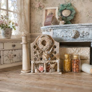 Könnte beinhalten: Ein Miniatur-Leuchtturm aus Holz neben einem dekorativen Gitter, das mit einem Rettungsring, einem Seestern und kleinen künstlichen Blumen verziert ist. Zwei klare Glasgefäße mit kleinen braunen und gelben Objekten stehen daneben.