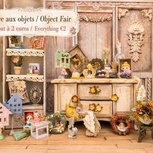 Könnte beinhalten: Eine Miniatur-Ausstellung mit einem Holzschrank und Regalen voller kleiner Dekorationsartikel, darunter winzige Häuser, Kränze, Figuren und eine gelbe Handtasche. Ein Schild oben lautet: Foire aux objets / Object Fair, Tout à 2 euros / Everything €2.