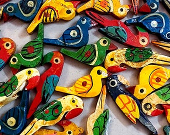 May include: A collection of colorful, wooden bird figurines in various poses. The birds are painted in bright hues of red, yellow, blue, and green, with black and white accents. The collection includes parrots and other bird species.