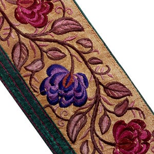 Könnte beinhalten: Besticktes Blumenband mit goldenem Hintergrund, mit burgunderroten und lila Blumen mit braunen Stielen und Blättern. Das Band hat einen grünen Rand. Dieser dekorative Besatz eignet sich für verschiedene Bastelprojekte.