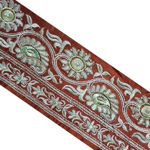 May include: A close-up of a brown fabric trim with silver embroidery. The trim features a paisley design and floral motifs.