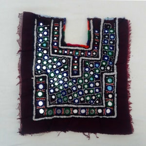 May include: A maroon fabric square with a geometric design embroidered with colorful thread and small round mirrors.