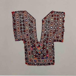 Könnte beinhalten: Dekoratives, besticktes Textil mit V-Ausschnitt. Der schwarze Stoff weist komplizierte Muster in Rot, Weiß und bunten Akzenten auf. Kleine, runde Spiegel sind in das Design eingenäht und reflektieren das Licht. Die Kanten sind mit einem roten Rand versehen.