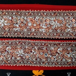 Può includere: Due file di bordino perlato argento e pesca con un retro in tessuto rosso. Il bordino è decorato con piccole paillettes e perline.