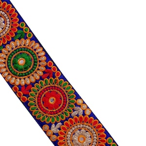 Può includere: Passamaneria in tessuto blu con motivi floreali ricamati colorati e paillettes argentate. La passamaneria presenta motivi circolari ripetuti con accenti rossi, verdi e gialli.