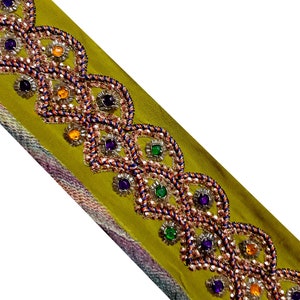 以下が含まれることがあります： オリーブグリーンの生地トリムで、オレンジ、ブルー、グリーンの宝石がついたビーズのデザインが施されています。トリムは波状の縁を持っています。