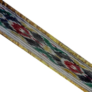 Può includere: Un nastro grigio e bianco con un bordo dorato e un motivo ikat colorato. Il nastro è tessuto con un motivo geometrico in tonalità di rosso, verde, blu e giallo.