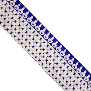 Pode incluir: Bordado branco com acabamento em veludo azul. O bordado apresenta um padrão repetitivo de pequenas flores.