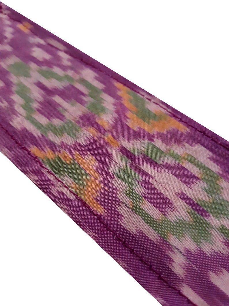 May include: Purple fabric with a green and orange ikat pattern. The fabric has a stitched edge.