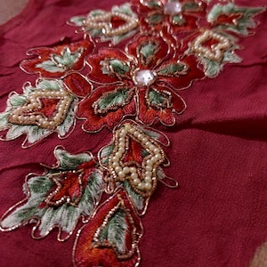 Puede incluir: Primer plano de una tela roja con un diseño de bordado floral. El bordado presenta cuentas y lentejuelas rojas, verdes y blancas.