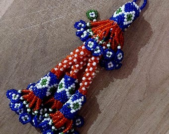 May include: A beaded tassel keychain with a blue, white, and green pattern. The tassel is made of small, colorful beads and has a loop at the top for attaching to a key ring.