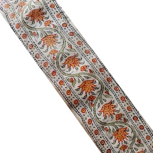 Puede incluir: Borde de algodón blanco con un patrón repetido de flores naranjas y hojas verdes. El borde tiene un borde negro y un fondo blanco.