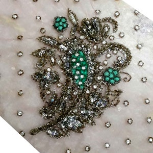 Puede incluir: Primer plano de una tela delicada de color rosa claro con un diseño floral bordado con lentejuelas plateadas y cuentas verdes.