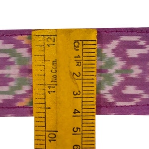 May include: Purple and green fabric with a repeating pattern, measured with a ruler in inches. The fabric is 6 inches wide.