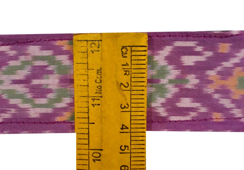 May include: Purple and green fabric with a repeating pattern, measured with a ruler in inches. The fabric is 6 inches wide.