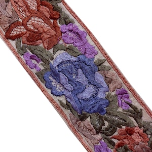 以下が含まれることがあります： 明るいベージュの背景に、密度の高い花柄の刺繍が施された装飾用の布製トリム。深みのある赤、鮮やかな紫、青の色合いで描かれた大きく詳細な花々と、濃い緑色の葉や茎が特徴的なデザインです。
