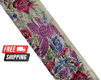 Pode incluir: Uma guarnição de tecido cinza com desenhos florais e de pássaros bordados em tons de rosa, roxo e azul. A guarnição apresenta um padrão repetitivo de rosas, folhas e um pássaro com as asas abertas.