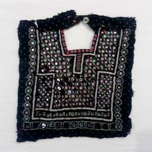 May include: A black fabric neckpiece with intricate embroidery featuring small mirrors and beads. The neckpiece has a small button at the top.