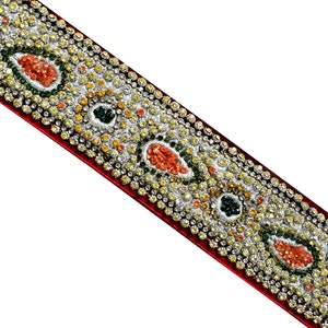 May include: A red fabric trim with a silver, green, and orange jeweled design. The trim is decorated with small, sparkling rhinestones.