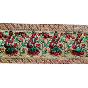 May include: Beige fabric trim with a repeating pattern of women in red, green, and brown dresses carrying pots on their heads. The trim has a brown and gold border.