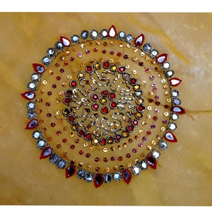 May include: A circular design with red, gold, and silver sequins and beads on a yellow fabric background.