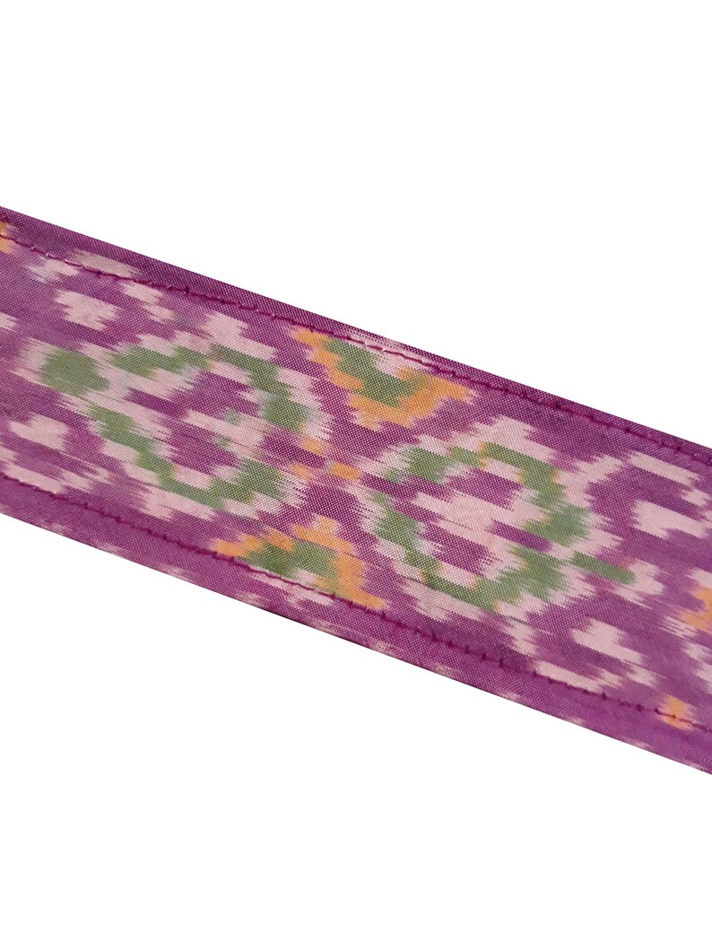 May include: A close-up of a purple fabric with a green, white, and orange ikat pattern. The fabric has a subtle sheen and a soft texture.