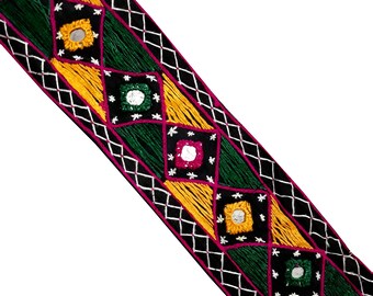 Pode incluir: Bordado preto, verde, amarelo e rosa com detalhes bordados e pequenos espelhos redondos. O bordado tem um padrão de diamante.