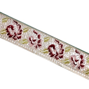 Könnte beinhalten: Nahaufnahme einer beige-weißen Borte mit Blumenmuster. Die Borte zeigt rote Samtblumen mit rosa und grünen Akzenten.