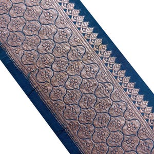 Può includere: Primo piano di una sezione di tessuto con un motivo floreale dettagliato in oro e uno sfondo blu scuro. Il motivo dorato presenta un motivo ripetuto di fiori stilizzati all'interno di un design geometrico. Il bordo ha un bordo decorativo.