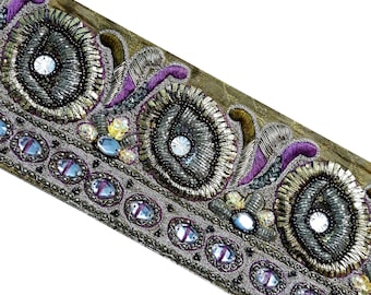 May include: A close-up of a decorative trim with gold, silver, and purple embellishments. The trim features a repeating pattern of beaded circles and ovals, with small, clear rhinestones scattered throughout.