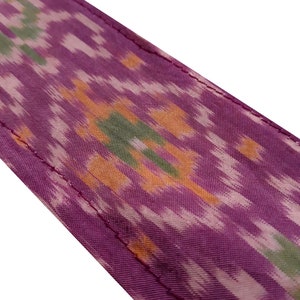 May include: Purple fabric with a colorful ikat pattern. The fabric has a subtle sheen and a soft texture.