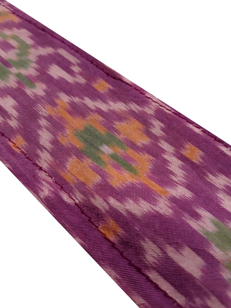 May include: Purple fabric with a colorful ikat pattern. The fabric has a subtle sheen and a soft texture.