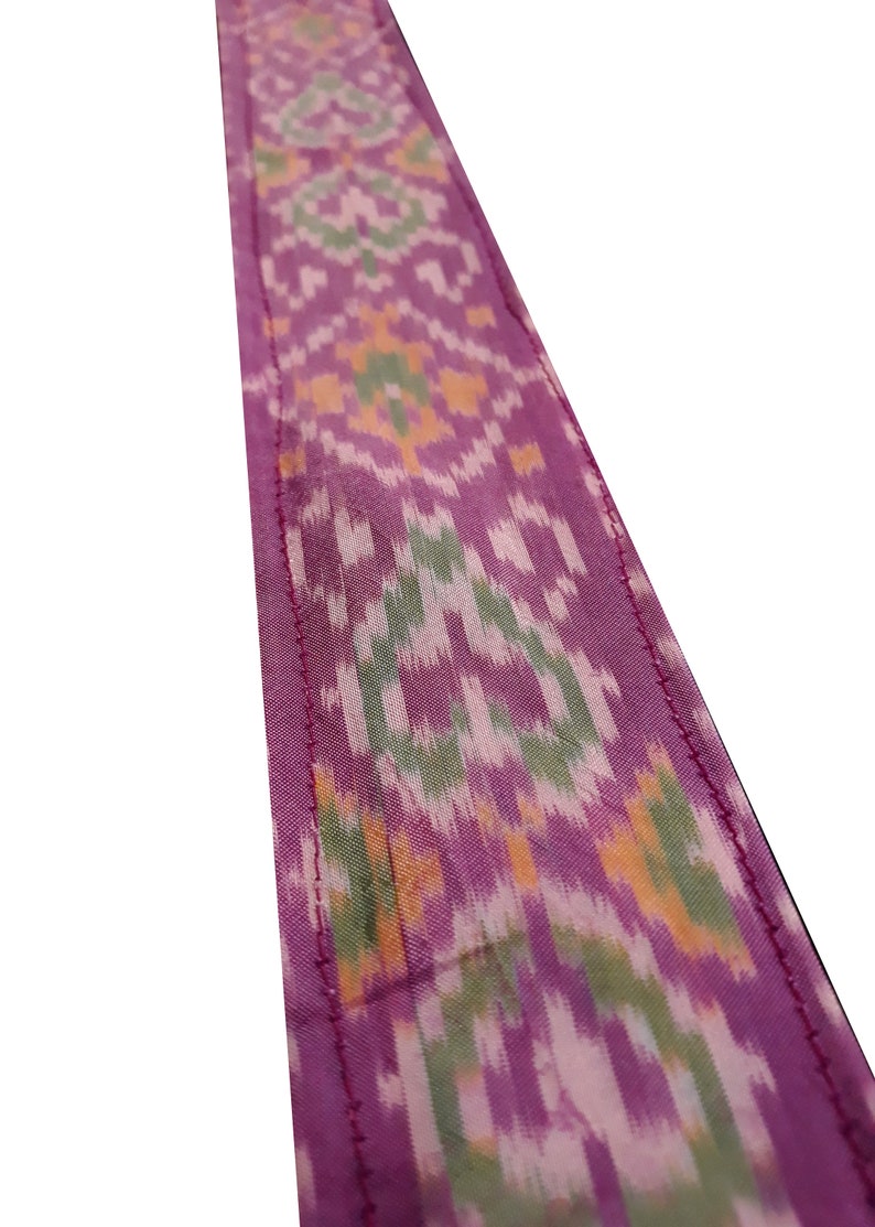 May include: A close-up of a pink fabric with a green, white, and orange ikat pattern. The fabric has a stitched edge.