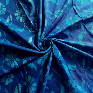 Könnte beinhalten: Blauer Stoff mit einem wirbelnden Muster aus türkisfarbenen Blumen. Der Stoff ist weich und hat einen dezenten Glanz.