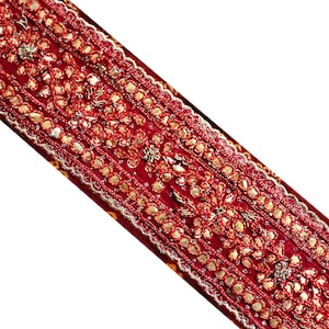 May include: Red fabric trim with gold embroidery and sequins. The trim features a repeating pattern of floral designs and small round beads.