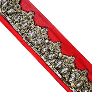 May include: Red fabric trim with a gold and silver beaded design. The trim features a repeating pattern of leaves and rhinestones.