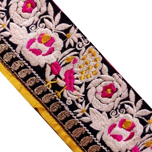 Può includere: Primo piano di un bordo ricamato decorativo con base nera, motivi floreali bianchi e rosa e bordo dorato. Il retro è giallo. Il ricamo è dettagliato e i colori sono vivaci.