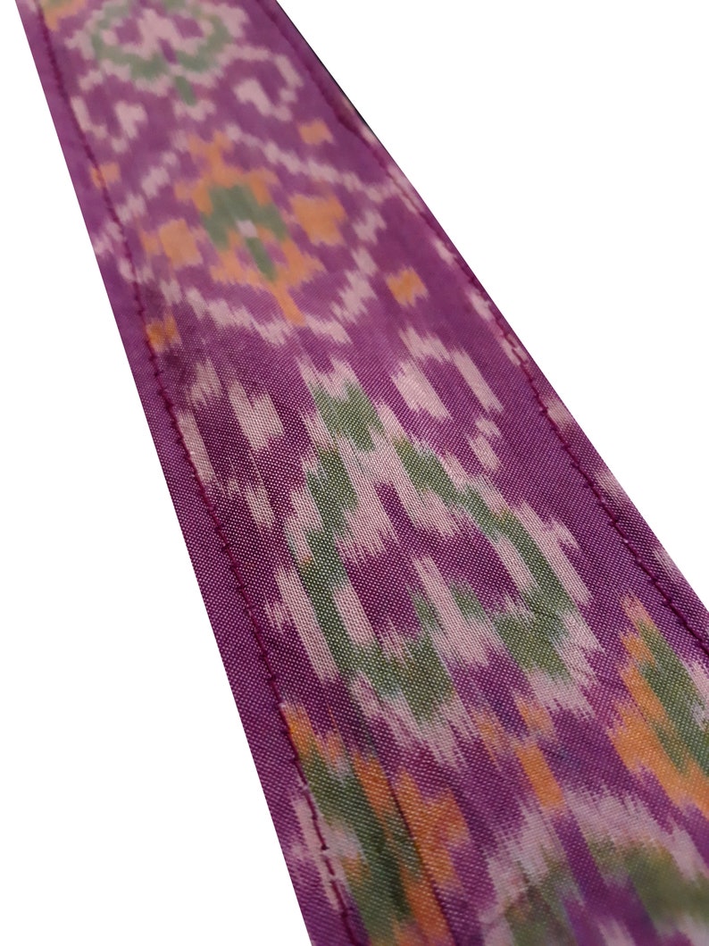 May include: Purple fabric with a green, orange, and white ikat pattern. The fabric has a stitched edge.