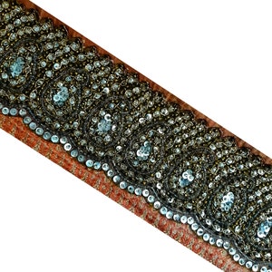 May include: A close-up of a brown and silver beaded trim with a scalloped edge. The trim is decorated with sequins and beads in a repeating pattern.