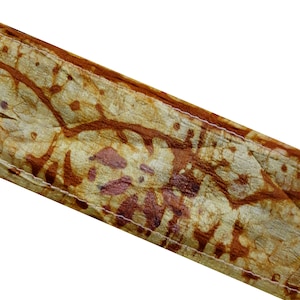 May include: A close-up of a brown leather strap with a white stitching detail. The leather has a mottled, brown and tan pattern.