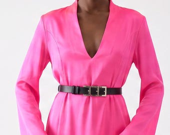 May include: A vibrant fuchsia dress with a V-neckline and long sleeves. The dress is cinched at the waist with a black belt and features a thigh-high slit. The model is standing in front of a white background.