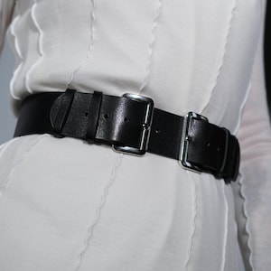 Może przedstawiać: Czarny skórzany pasek z srebrną klamrą i podwójnymi paskami.