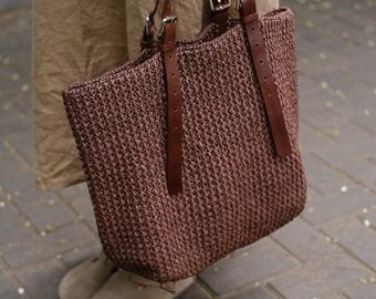 May include: A brown woven tote bag with leather straps and buckles. The bag is large and has a wide opening.